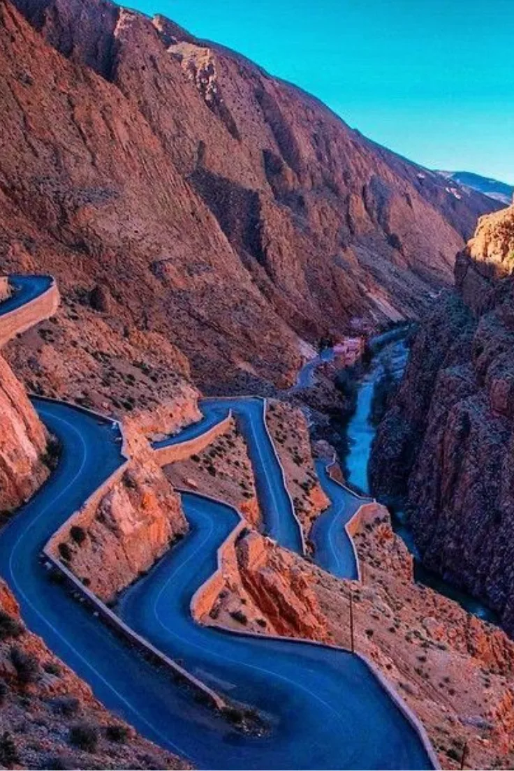 Aerial view of a winding road and river in a red rock canyon in the Atlas Mountains of Morocco