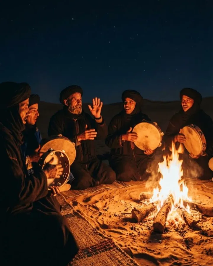 Gnawa musicians playing drums around a campfire at night in the Sahara