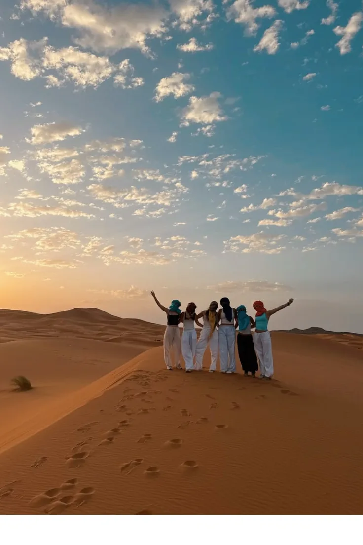 Group of travelers with arms raised on the Zagora desert dunes at sunset