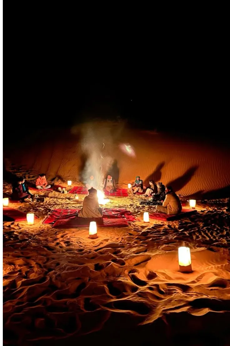 Guests around a campfire with lanterns at night in a Zagora desert camp