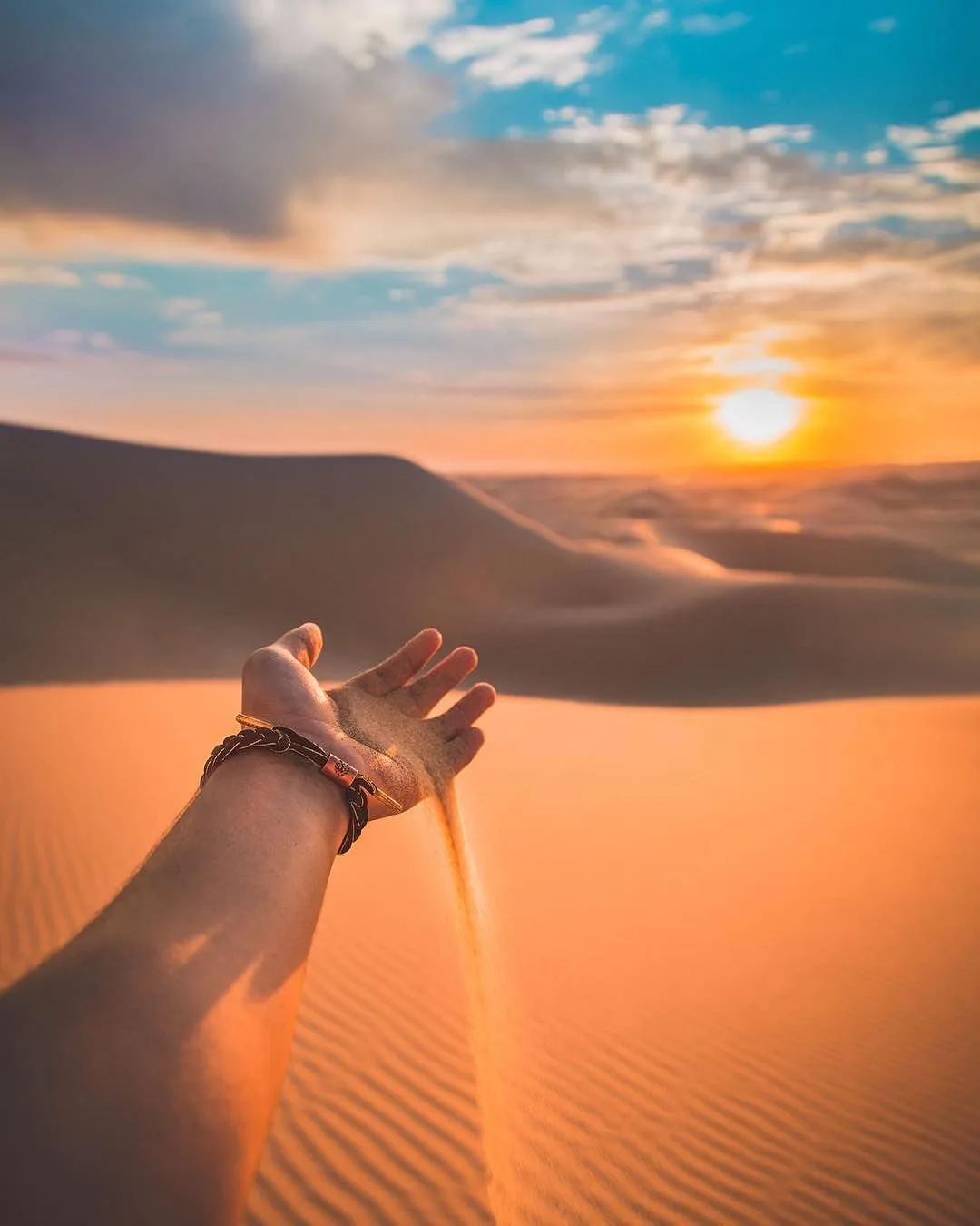 Hand letting golden desert sand fall at sunset in the Sahara