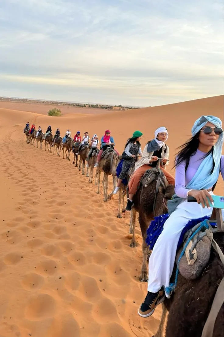 Travelers riding a camel caravan across the Zagora desert dunes