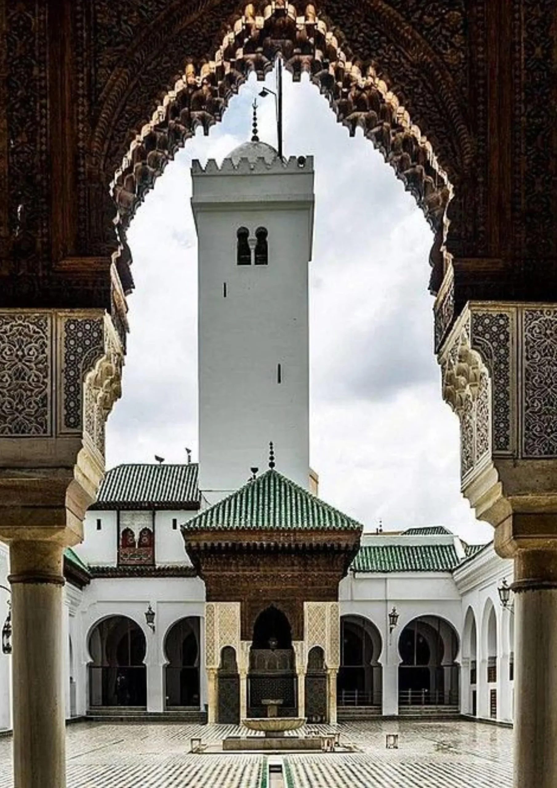 White minaret and green-tiled roof framed by carved plasterwork arches in Fes