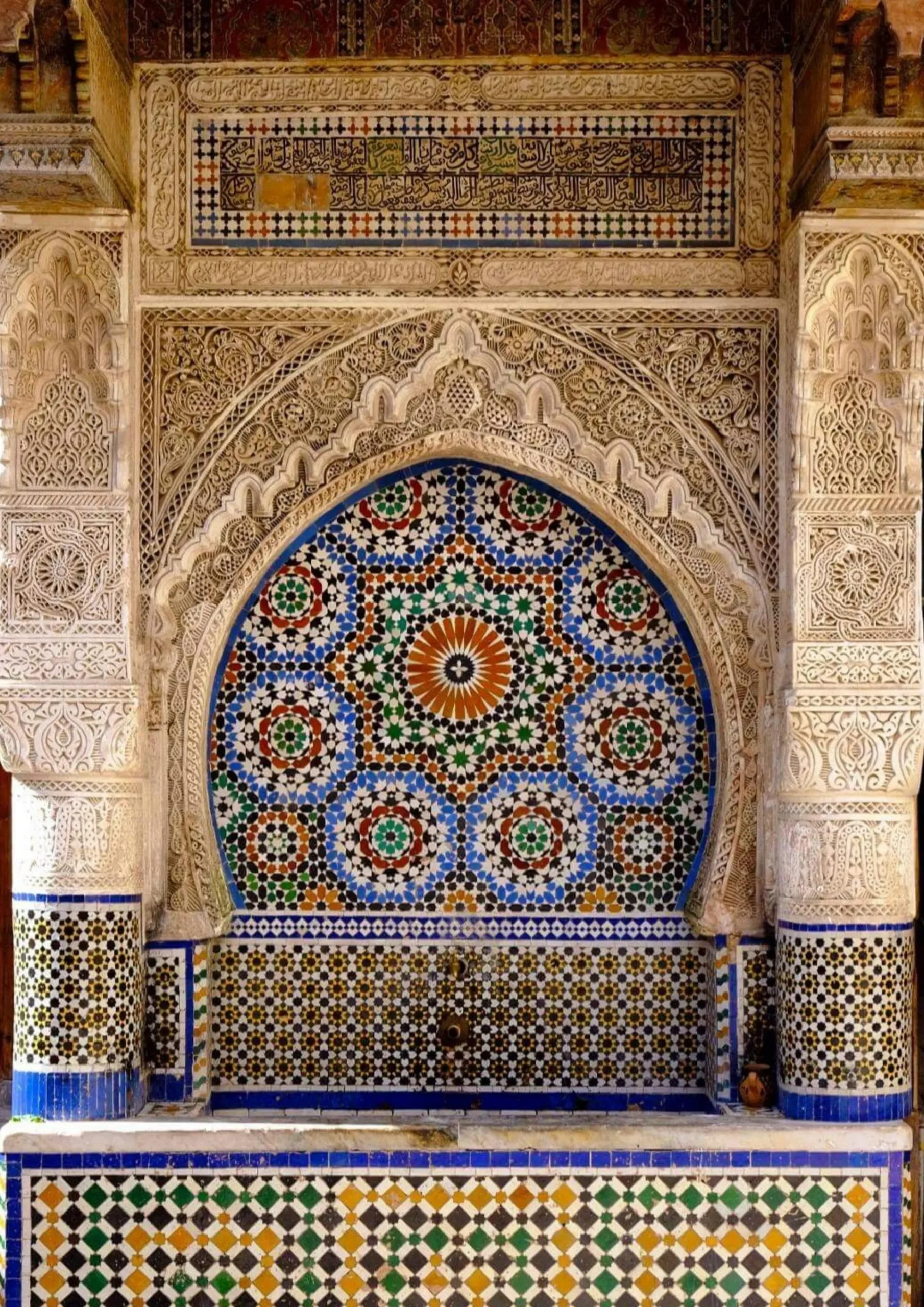 Zellige mosaic rosette set in a carved plaster arch in the Fes medina